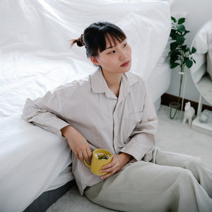 Asian woman laying next to bed wearing beige pajama shirt and pants